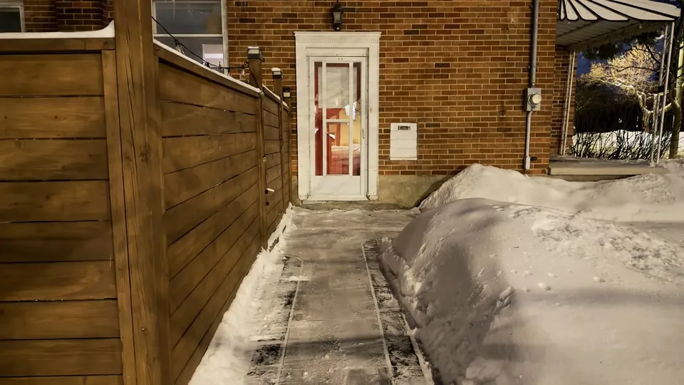 Cleared narrow walkway beside a wood fence and a brick house